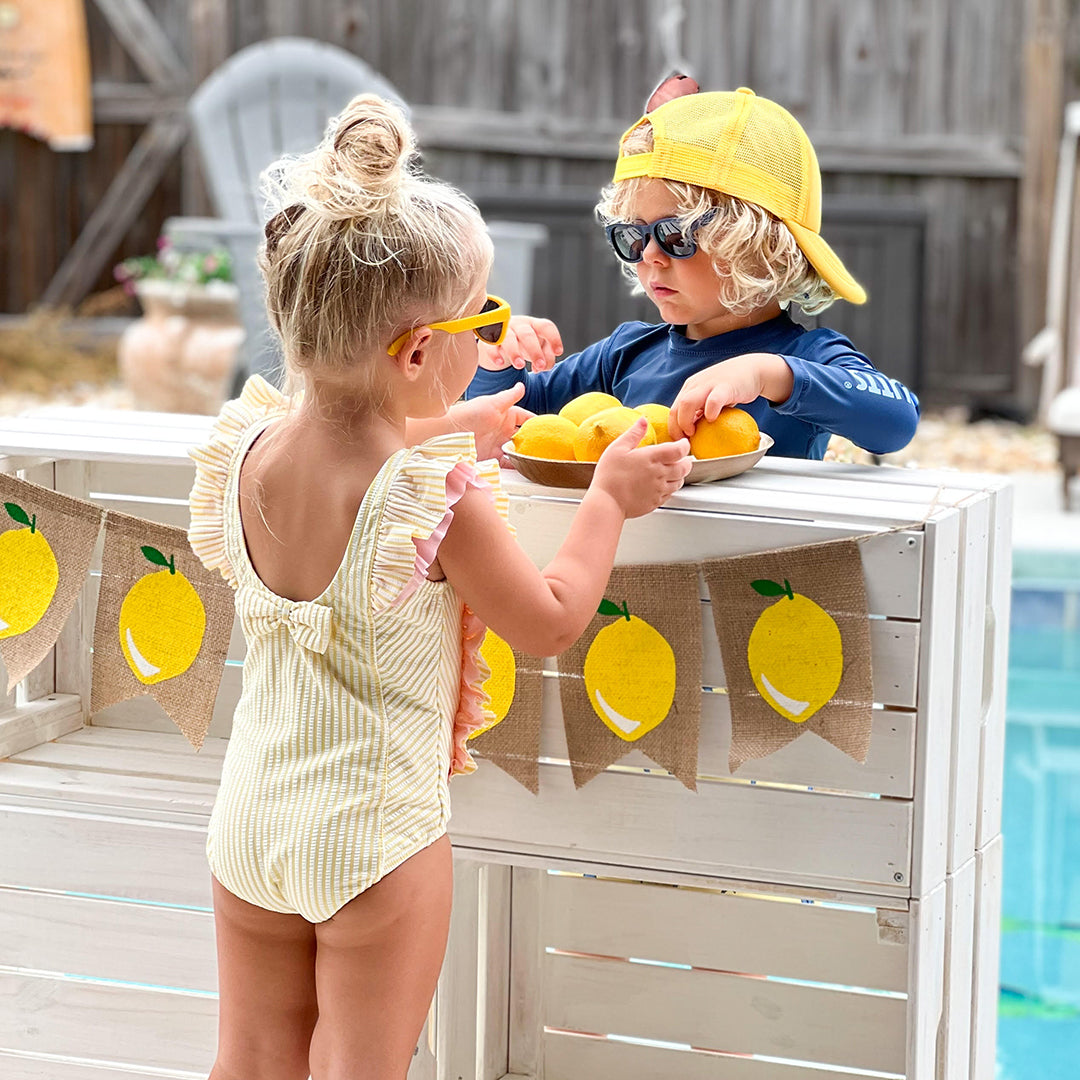 RuffleButts Girls Seersucker One Piece with Roshambo Yellow Sunglasses - HoneyBug 